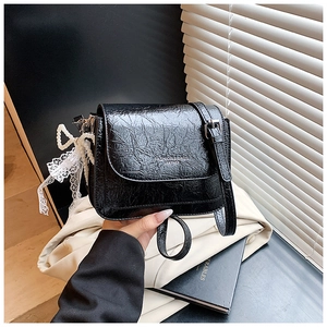 Détail du sac bandoulière noir avec texture cuir craquelé et breloque nœud en dentelle