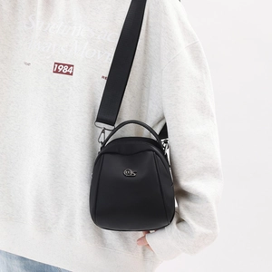 Detail of black mini shell bag with wide nylon strap and silver logo on a model
