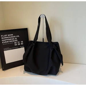 Detail of black tote bag with knot strap design on a minimalist display stand