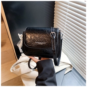 Gros plan sur un sac bandoulière en cuir plissé noir avec breloque perle et rabat