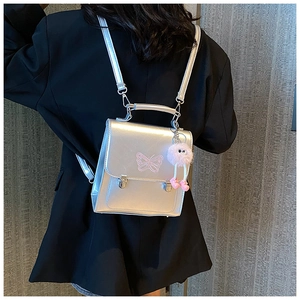Détail du sac à dos argenté métallisé avec broderie papillon rose et breloque peluche