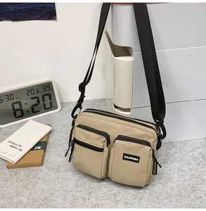 Close-up of khaki nylon crossbody bag with multiple zipper pockets and wide black strap