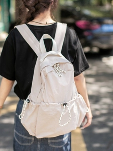 Back view of model wearing a beige multi-pocket travel backpack in outdoor sunlight