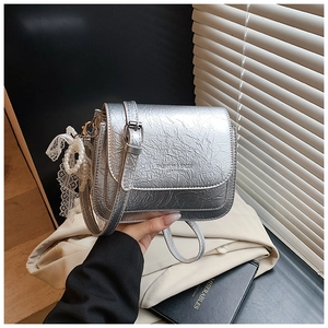 Détail du sac bandoulière argenté texturé avec breloque en perles et logo texte gaufré