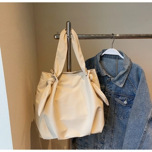 Detail of beige tote bag with unique knot handle design hanging next to denim jacket