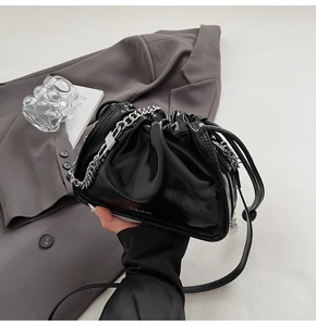 Detail of black glossy patent leather bucket bag with silver chain and drawstring closure