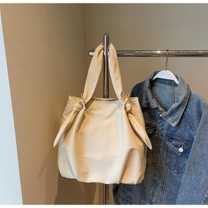 Detail of cream pleated tote bag with knot strap hanging next to a denim jacket
