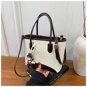 Détail d'un sac cabas bicolore avec pendentif de poupée et finitions métalliques dorées