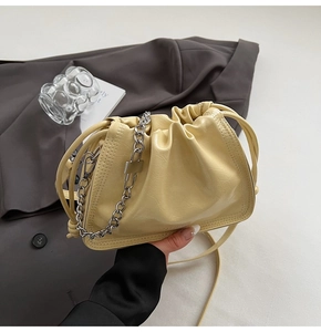 Detail of pale yellow bucket bag with metallic chain and elegant pleated PU texture