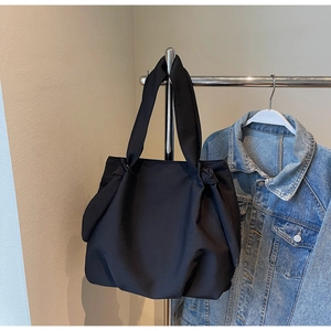 Detail of minimalist black tote bag with knotted strap design and spacious nylon structure
