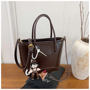 Gros plan d'un sac cabas en cuir marron foncé avec un charm de poupée et une bandoulière