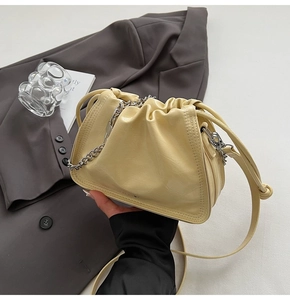 Detailed close-up of cream leather bucket bag with silver chain and drawstring closure