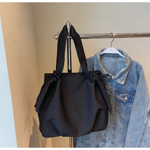 Detail of minimalist black tote bag featuring a decorative knotted bow handle and canvas texture