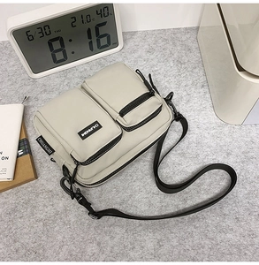 Detail view of a grey nylon crossbody bag with dual zipper pockets and adjustable strap