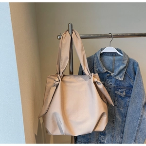 Detail of a beige leather tote bag with unique side knots hanging by a denim jacket