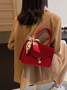 Elegant red bridal handbag with gold chain strap and silk scarf worn by a model