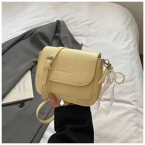 Détail du sac bandoulière en cuir plissé jaune avec breloque nœud en perle et dentelle
