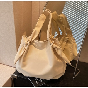 Detail shot of a cream tote bag featuring a decorative knot accent and soft leather texture