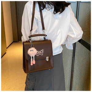 Détail du sac à bandoulière marron foncé avec papillon en métal et breloque peluche rose