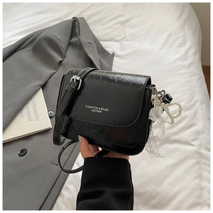 Détail du sac en cuir plissé noir brillant avec chaîne en perles et nœud en dentelle