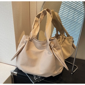 Detail of a beige canvas tote bag featuring a knotted handle and spacious fabric design