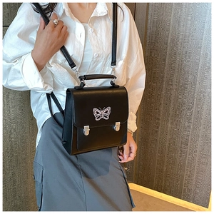 Détail du sac à dos en cuir noir avec écusson papillon rose et boucles métalliques argentées