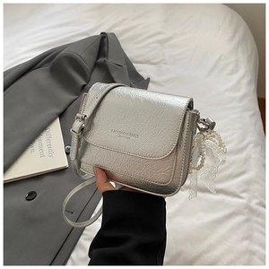 Détail du sac à bandoulière argenté avec texture froissée et pendentif perle dentelle