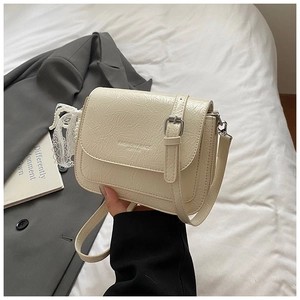 Détail du sac en cuir verni blanc crème avec breloque en perles et dentelle et logo