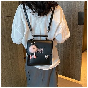 Détail d'un sac à dos en cuir PU noir avec logo papillon rose et breloque pelucheuse