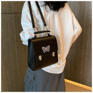 Détail d'un sac à dos noir avec broderie papillon rose porté par un mannequin en chemise