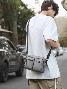 Outdoor grey multi-pocket nylon crossbody bag worn by male model in urban street setting