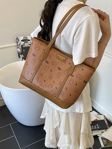 Braune Einkaufstasche mit Bärenprint und Goldlogo, von einem Model an der Schulter getragen