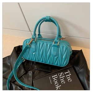 Detail of turquoise patent leather handbag with geometric V-shaped pleats on leather jacket