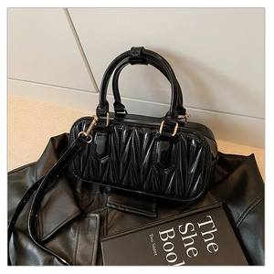 Close-up of black patent leather handbag with quilted wavy texture and gold metal hardware