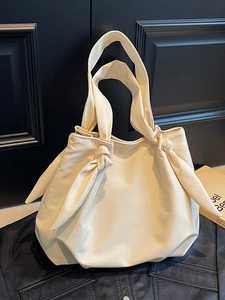 Minimalist cream white tote bag with decorative knot handles on black leather surface