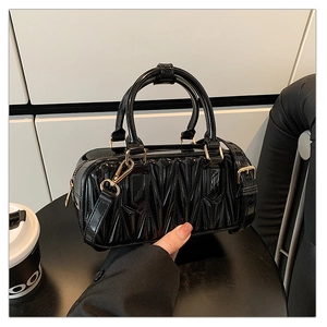 Detail view of glossy black patent leather crossbody bag with matelassé texture and gold hardware