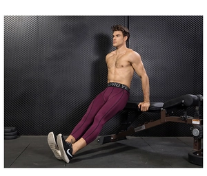 Men's burgundy compression leggings in gym setting showing flexible fabric and gray waistband