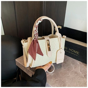 Détail d'un sac à main tressé crème avec foulard floral et fermoir tournant en métal doré