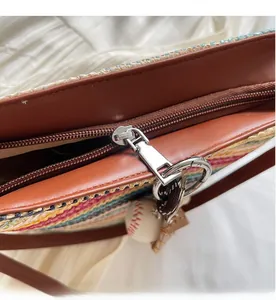 Detail of smooth metal zipper and brown leather trim on striped woven tote bag