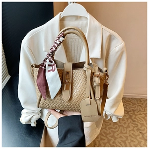 Détail du sac seau tissé marron clair avec poignées en cuir et foulard en soie décoratif