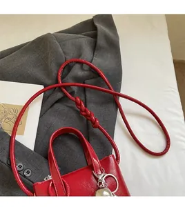 Dettaglio della borsa rossa lucida con tracolla lunga, nodo decorativo e ciondolo in metallo