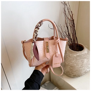 Détail d'un sac seau rose tressé avec poignée en foulard de soie et étiquette de mode
