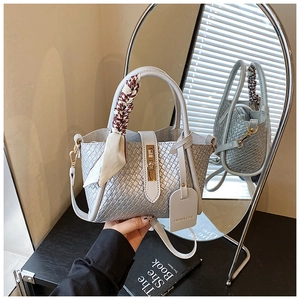 Détail du sac seau tressé gris avec fermoir doré et foulard pied-de-poule au manche