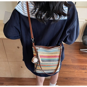 Detail of colorful striped woven tote bag featuring leather strap and baseball pendant charm