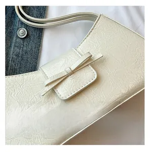 Detail of cream white pleated shoulder bag with leather bow and silver metal hardware