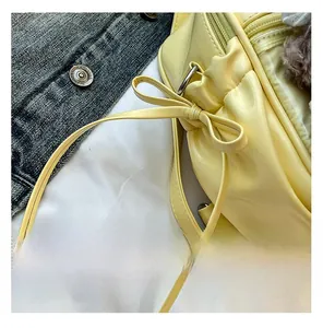 Detail of light yellow backpack showing drawstring bow design and silver metal D-rings