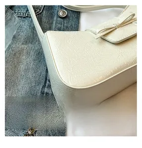 Detail of white crinkled leather shoulder bag with decorative bow and premium texture