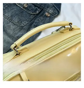 Detail view of cream yellow handbag featuring fine stitching and glossy metallic hooks