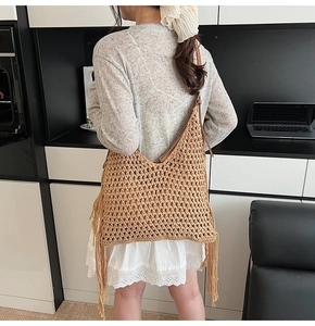 Detail of hand-woven hollow knit bag with long tassels and brown leather strap