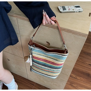 Detail of colorful striped straw tote bag with brown leather handles and baseball charm